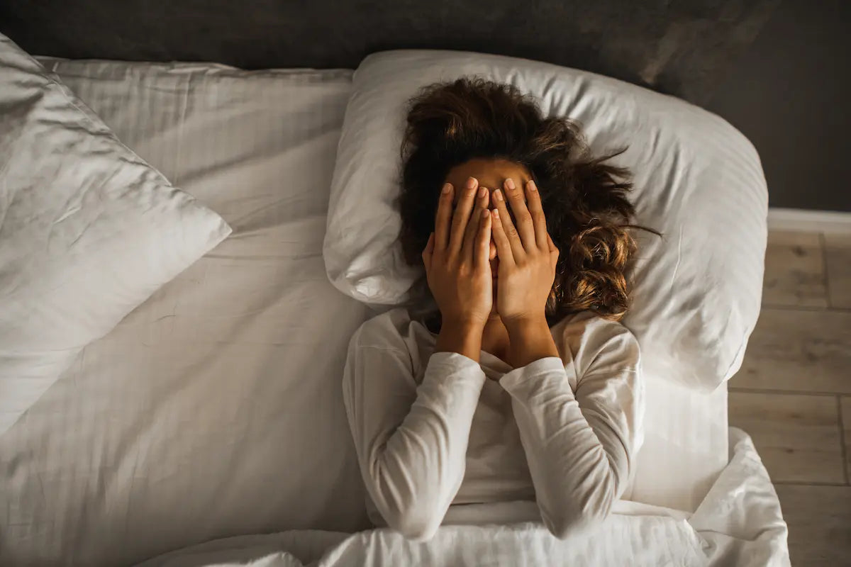 Femme allongée, mains sur le visage, signe de fatigue ou trouble du sommeil.