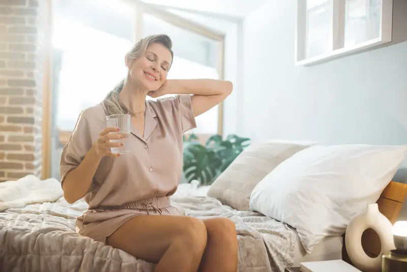 Femme en pyjama buvant de l’eau pour soulager les symptômes de la périménopause