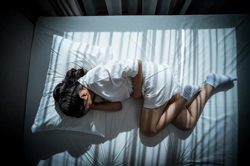 Femme recroquevillée sur un lit à cause de douleurs menstruelles