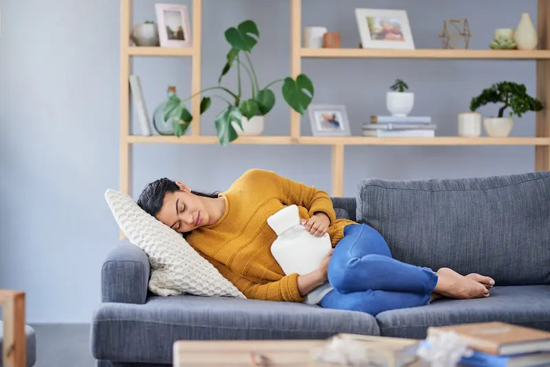 Femme allongée sur un canapé avec une bouillotte pour soulager ses règles douloureuses