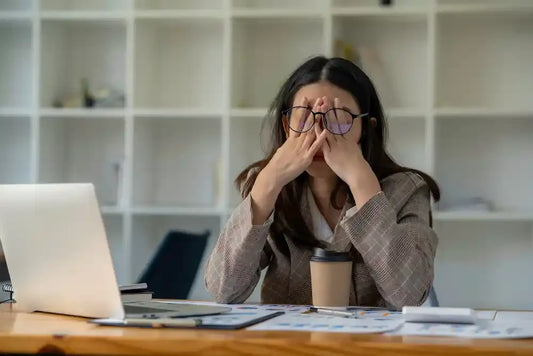 Femme fatiguée au bureau se frottant les yeux devant son ordinateur.