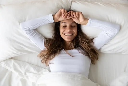 Femme souriante s’étirant dans son lit après une bonne nuit de sommeil