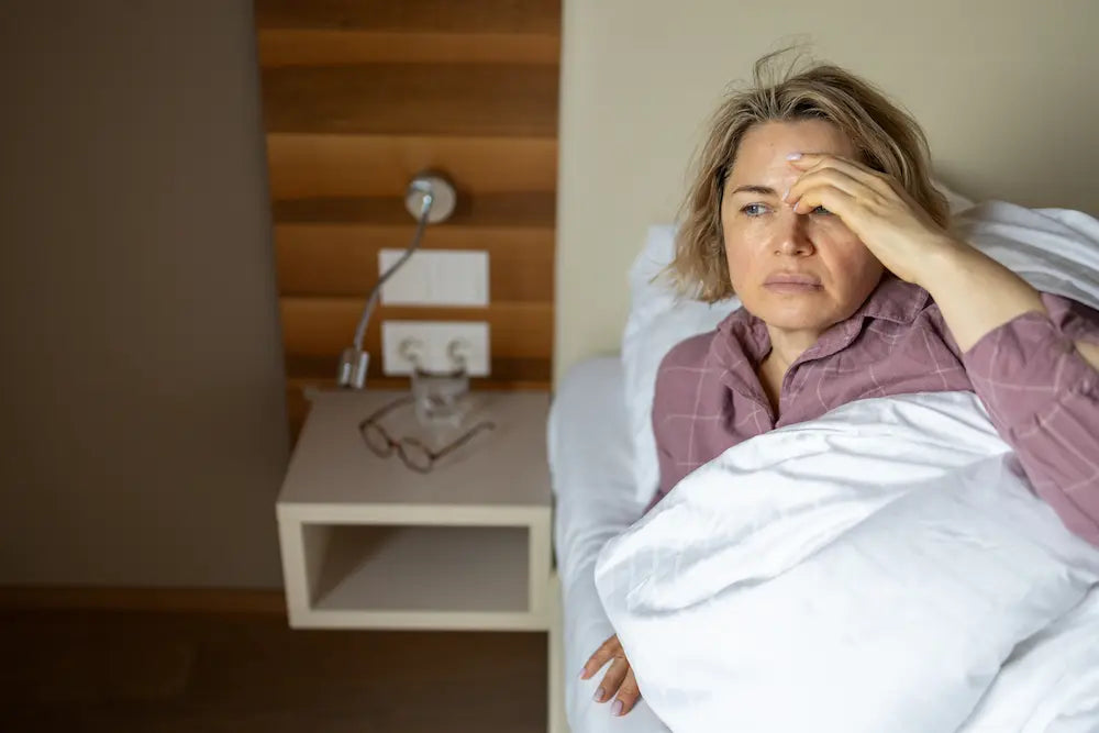 Une femme dans son lit avec un mal de tête à cause de la ménopause
